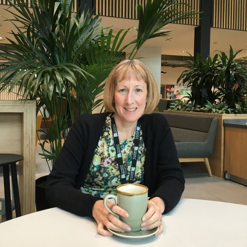 Nicky Sugar sitting at a table in the Senate House café area, holding a cup of coffee